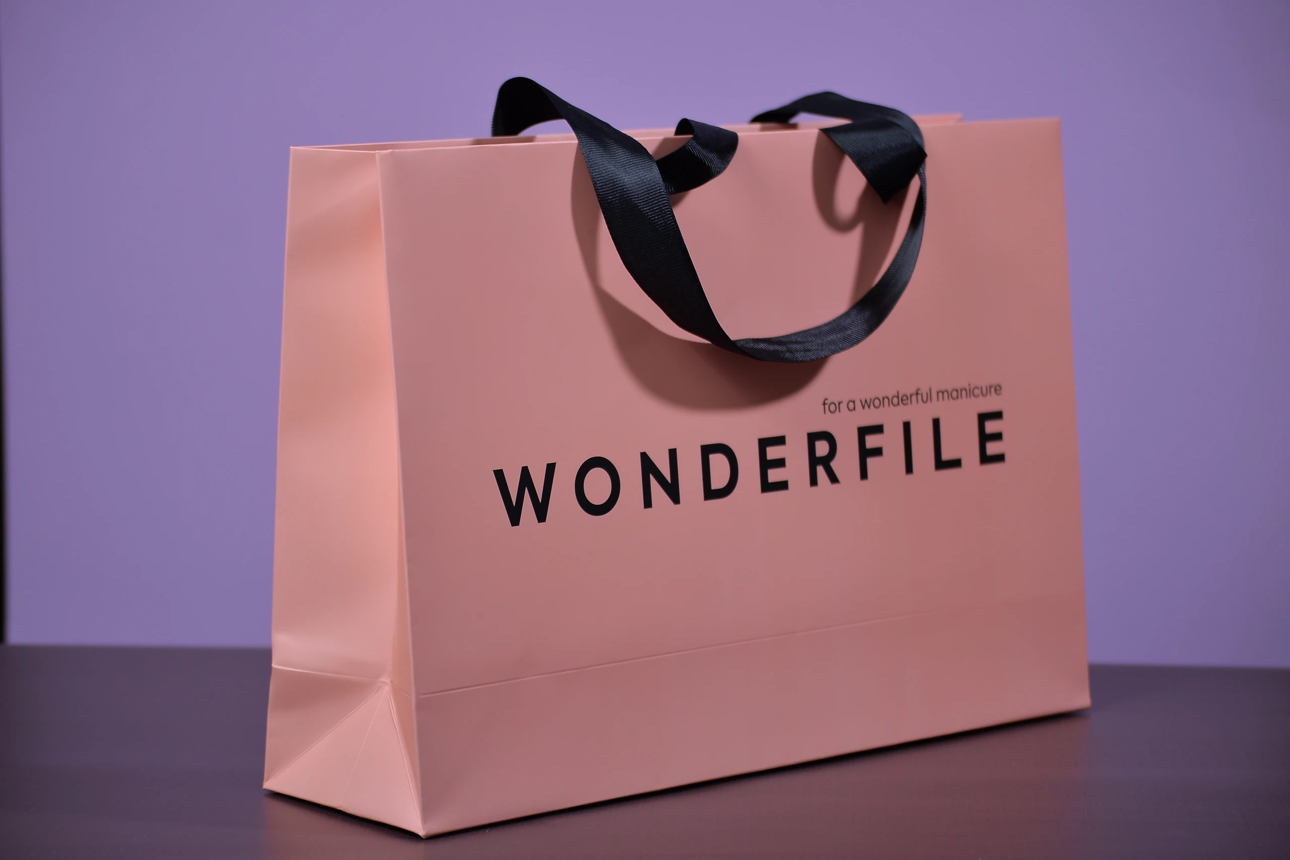 Персиковий паперовий пакет WONDERFILE з чорним логотипом, слоганом і складеною боковиною.